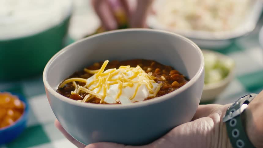 Someone is placing toppings onto a bowl of chili