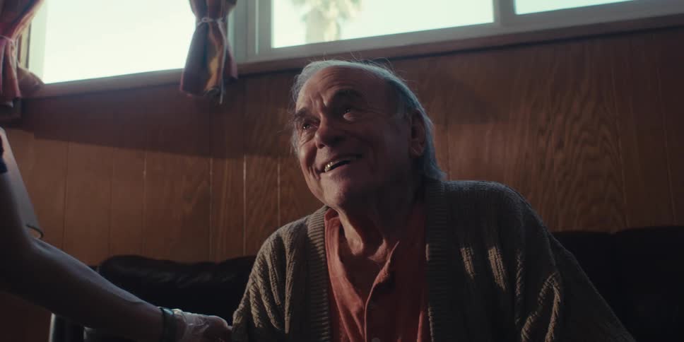 A medical professional is speaking and laughing with an elderly man in his home