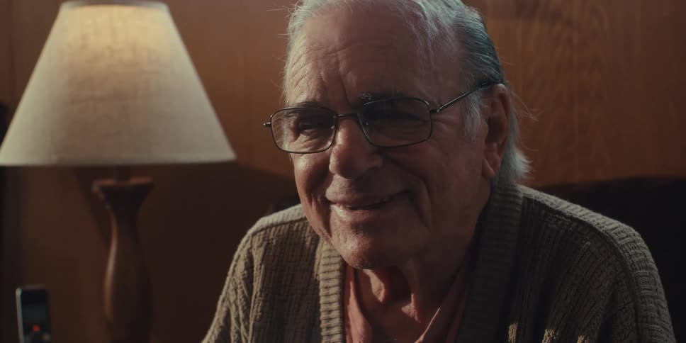 An elderly man is smiling and sitting in a chair
