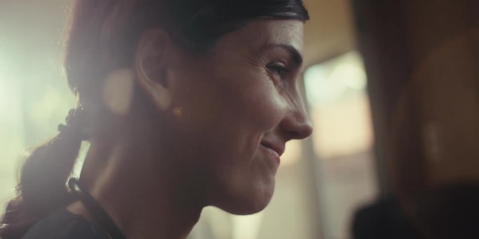 A health care professional with dark hair pulled back in a ponytail wearing a dark top and a stethoscope around her neck looking towards the right with a slight smile