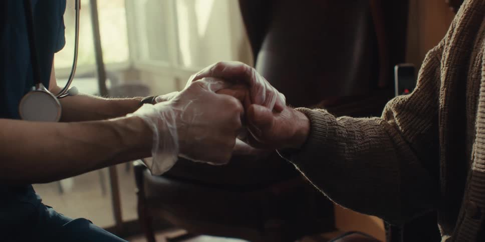 Medical professional comforts an elderly patient during a home healthcare visit by holding his hand
