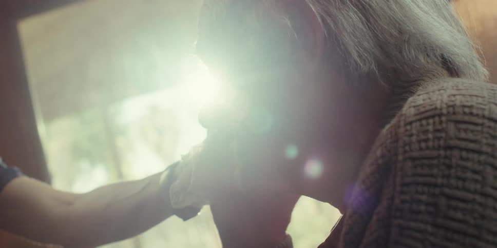 An elderly mans profile is seen as someone touches his face with bright light streaming in from the side