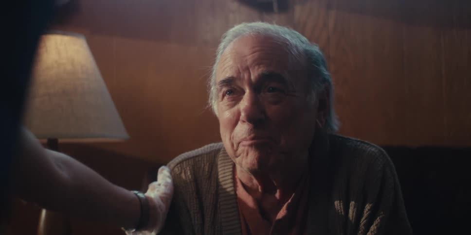 Elderly man sitting talking to a person who is patting his shoulders