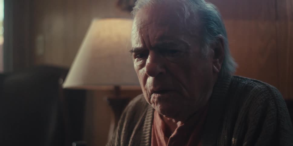 Elderly man begins to look downcast while sitting in a living room during the daytime