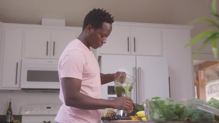 The man is pouring a smoothie in his kitchen