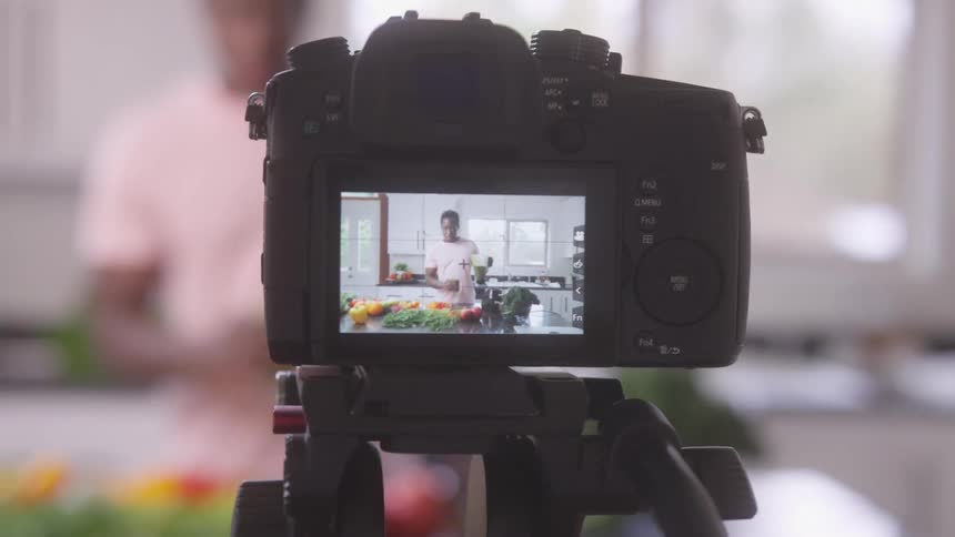 A person films a cooking scene in a kitchen with vegetables and ingredients arranged on the counter