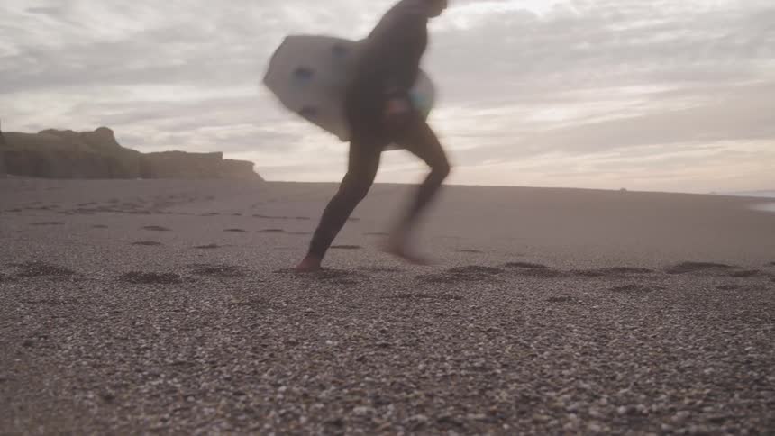 A person is running on the beach with their surfboard
