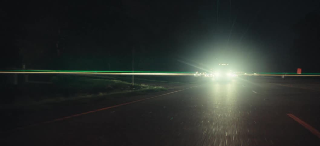Car headlights glare as the vehicle drives along a highway at night