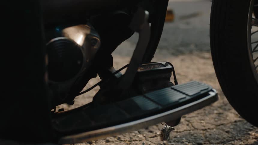 A person puts their foot on the footrest of a motorcycle with an eagle head charm hanging from the bottom