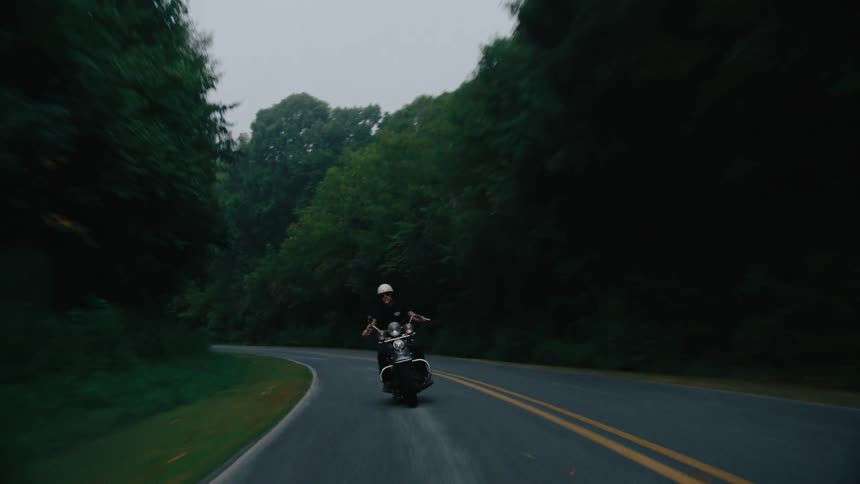A motorcyclist navigates a curving road bordered by lush dense forest