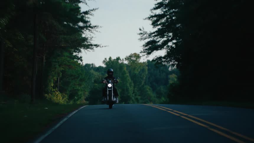 Person riding a motorcycle on a road surrounded by trees