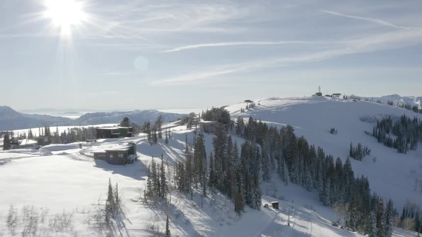 A serene snowy mountain range dotted with cabins surrounded by dense woodland under a vibrant morning sky