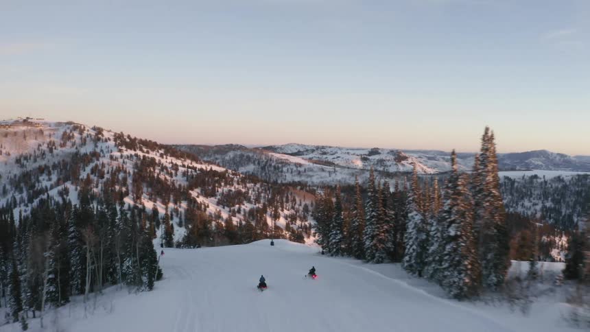People riding snowmobiles down a snow mountain