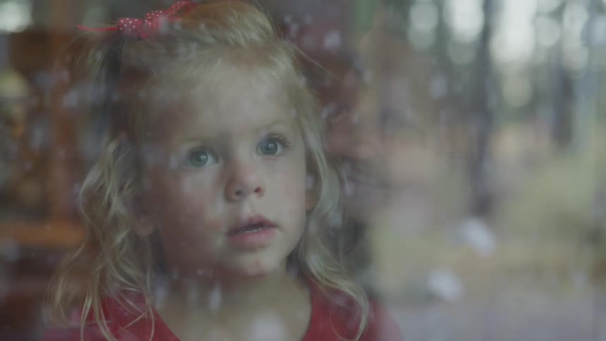Little girl looking out the window at falling snow