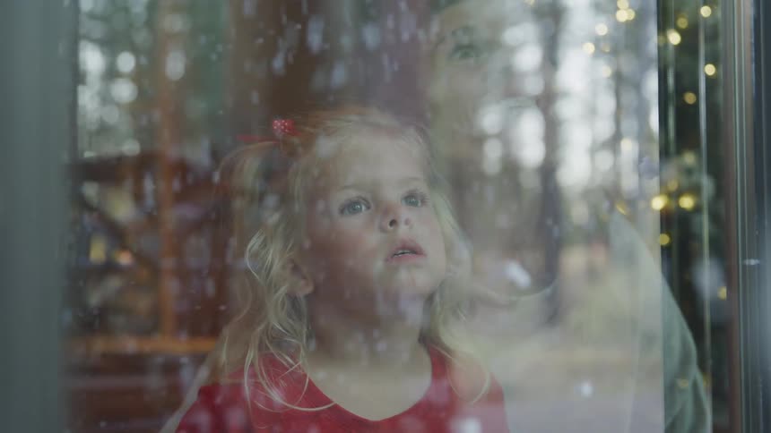 Mother and daughter looking out the window of a house snow falling