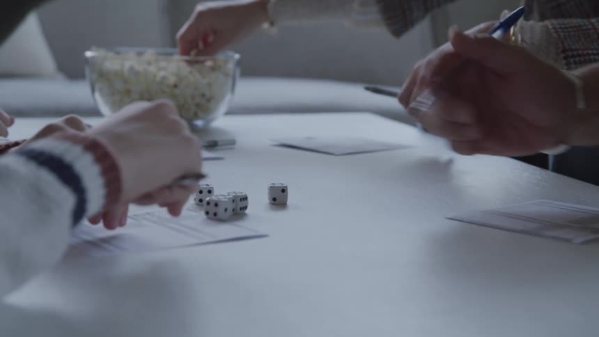 Hands of four people on a table eating popcorn and playing dice game