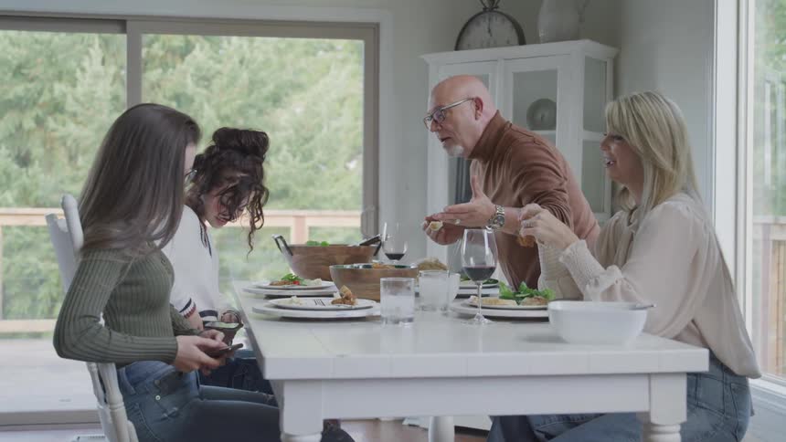 Father telling his teenage daughters to put away their cell phones while sitting at a table set with lunch