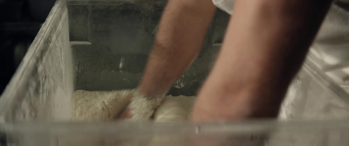 A baker is mixing a large amount of flour in a container by hand