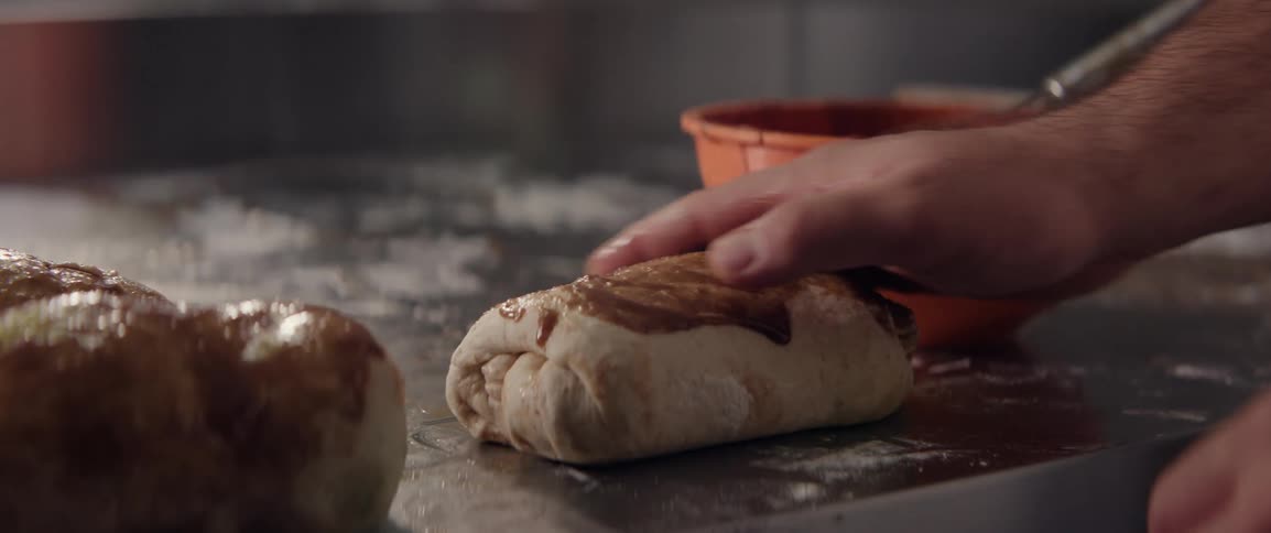 Close up of a hand pouring sauce into raw bread dough