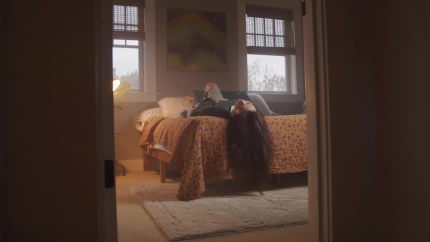 A teenage girl is resting on a bed in her bedroom