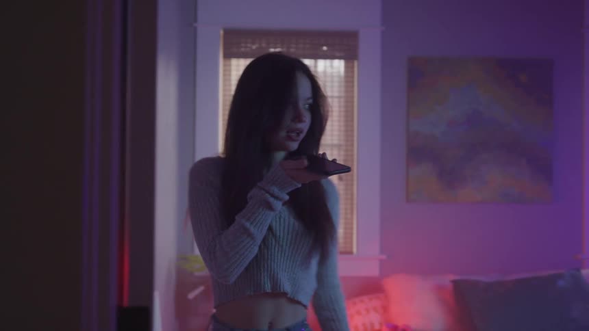 A female teen is pacing around the living room and talking on cellphone