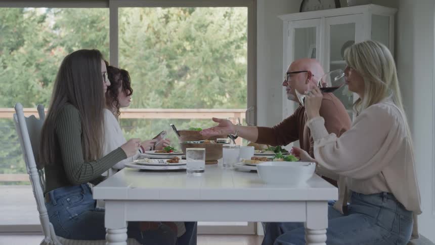 A family of four enjoy a meal at a dining table with a panoramic view of a lush green forest through a large window