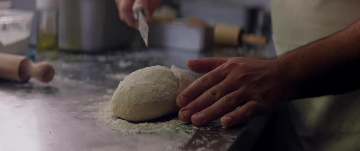A restaurant chef is cutting dough with a knife