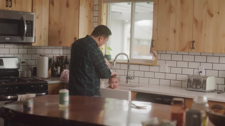 An adult is bathing a baby in a kitchen sink in a modern home setting