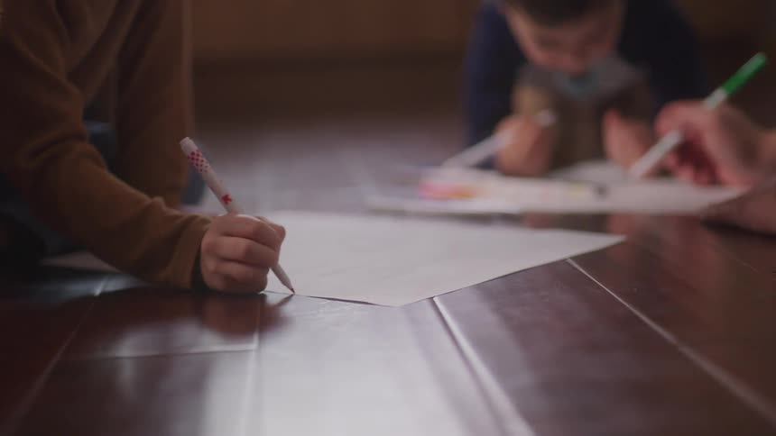 Two children on the floor drawing on white sheets of paper