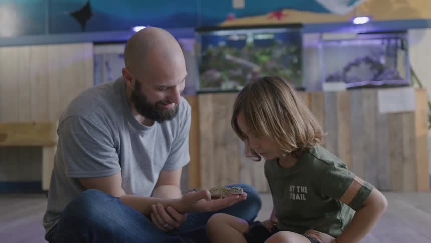 A man is showing a child a small lizard