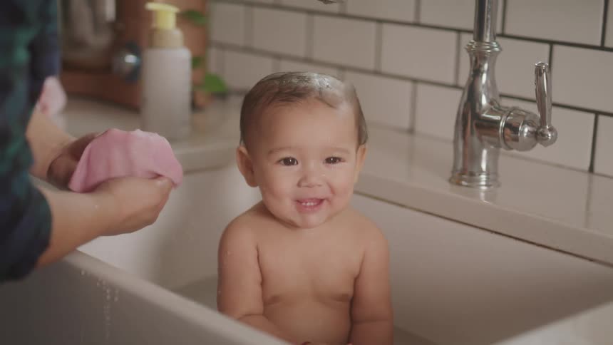 Baby in a bathtub taking a bath accompanied by an adult