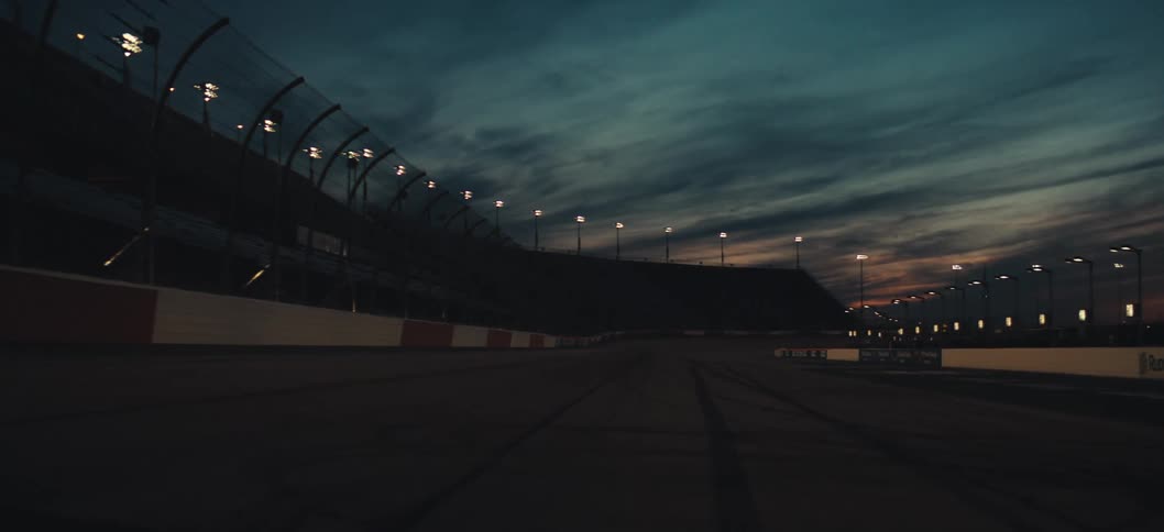 The sun sets over a racetrack on a mostly cloudy evening