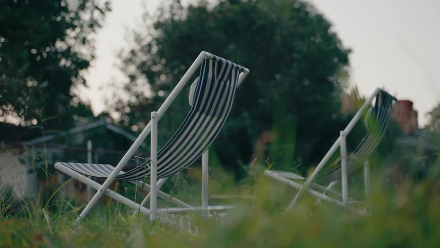 Two green and white striped lawn chairs sit in the backyard of a house