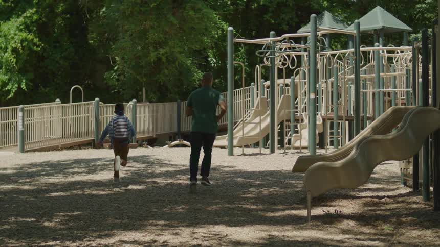 A father and son are running on a playground on a sunny summer day