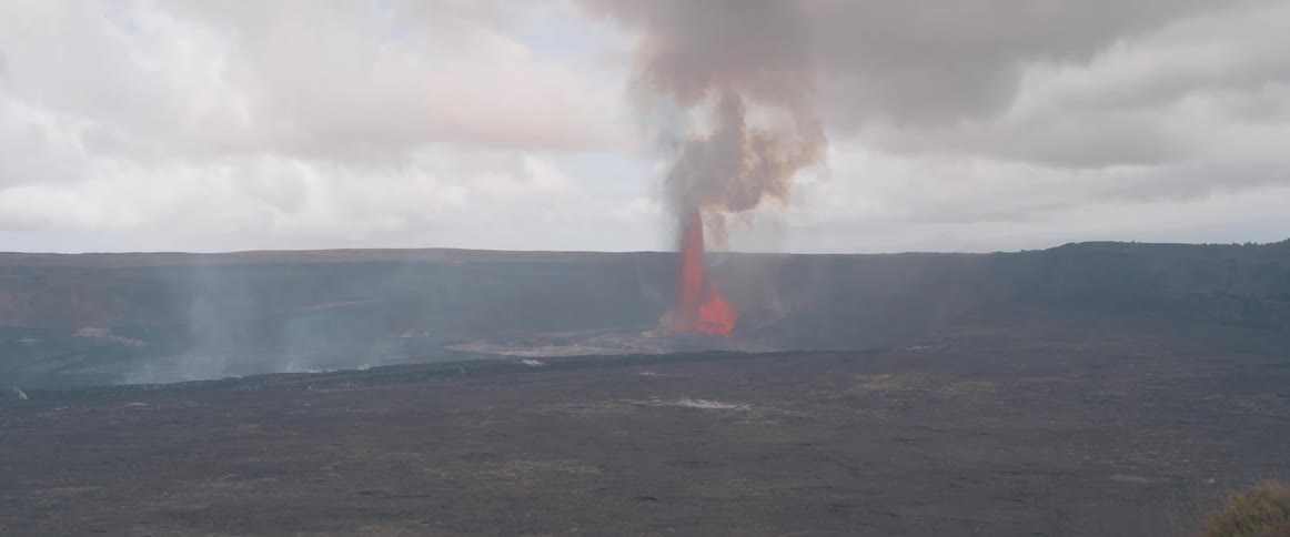 A volcanic eruption produces thick smoke plumes on a cloudy day