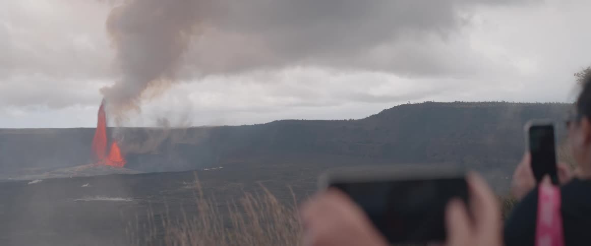 Tourists photographing an erupting volcano on the horizon