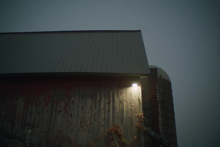 A silo stands near a barn on a foggy evening