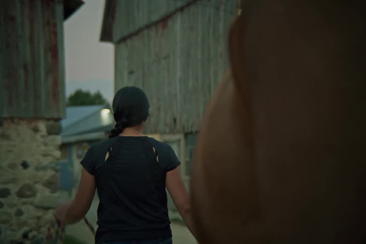 Woman walking towards a ranch and leading a horse with her