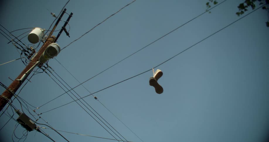 Tennis shoes hanging from wires overhead near a telephone pole under a dull blue sky