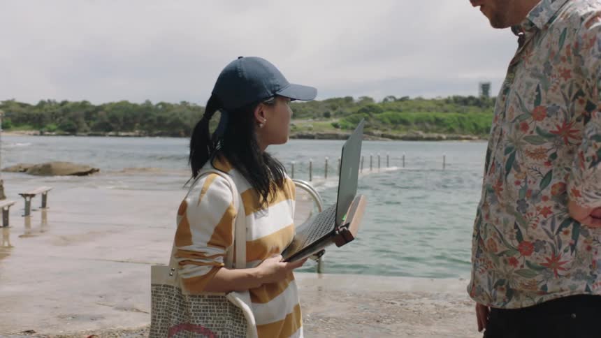 A woman talks with a man while holding a laptop