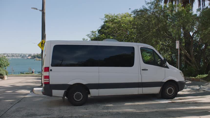 Man parks a van at a park across the water from the city and walks to the rear to open its door