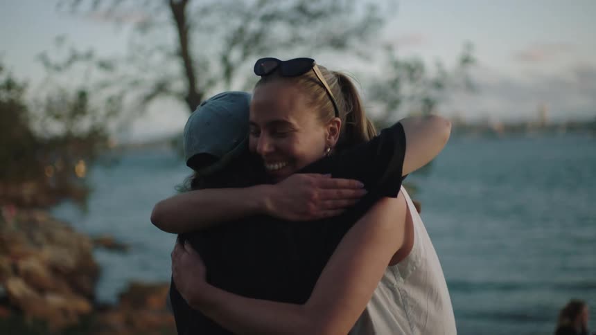 Group of women outdoors by the sea hugging each other and one person filming with a camera