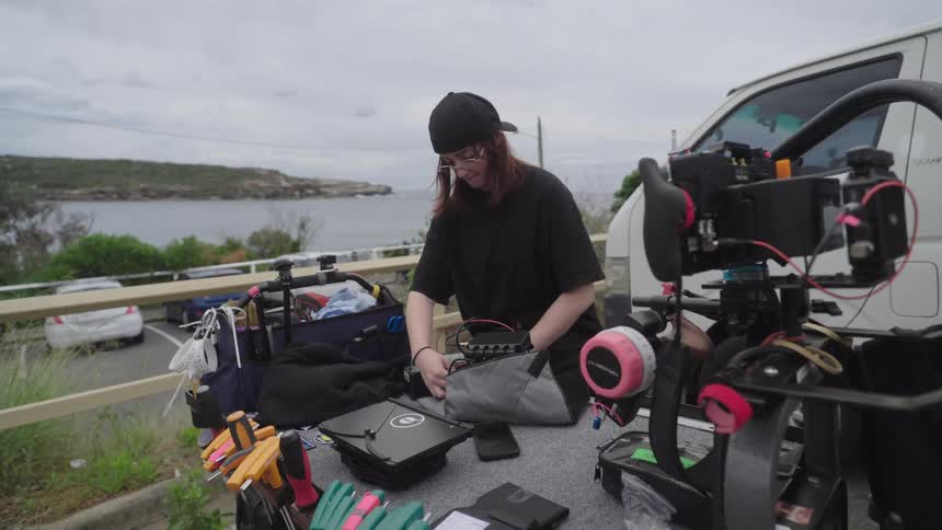 Member of the film crew accesses the film equipment placed on a table in a coastal parking lot
