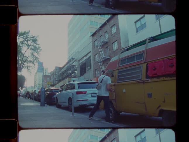 A man walks down a city sidewalk and opens the door to an old yellow van