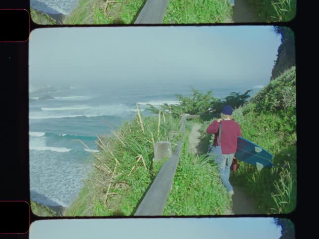 A man carries his surfboard on cliff by the shore