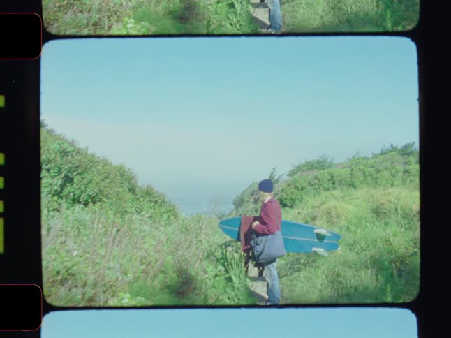 Man in the middle of a trail near the sea holding a surfboard