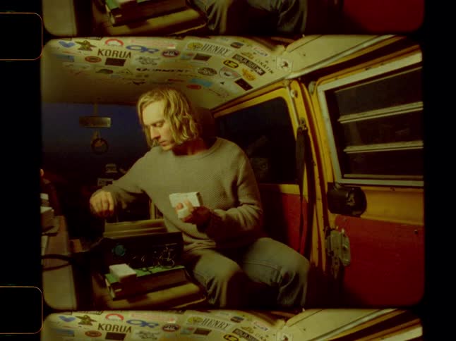 Man loads film slides into a slide projector while sitting in the back of a van at night