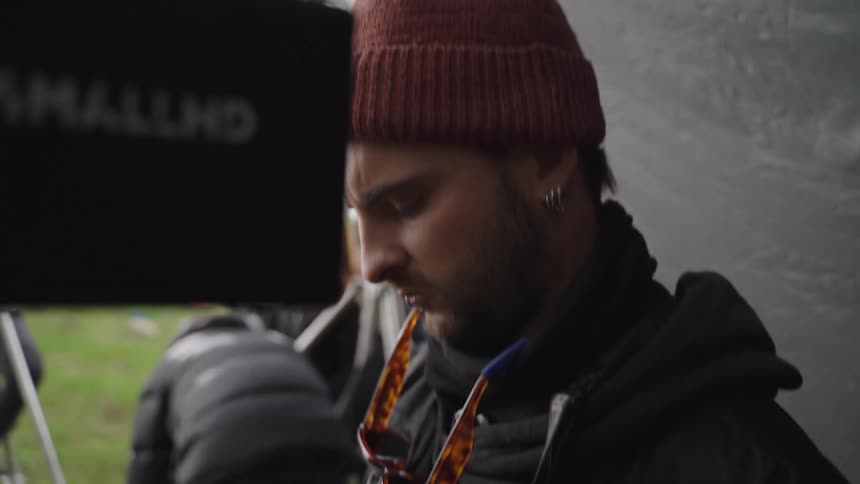 A film crew member in a beanie operates a remote focus controller on an outdoor set