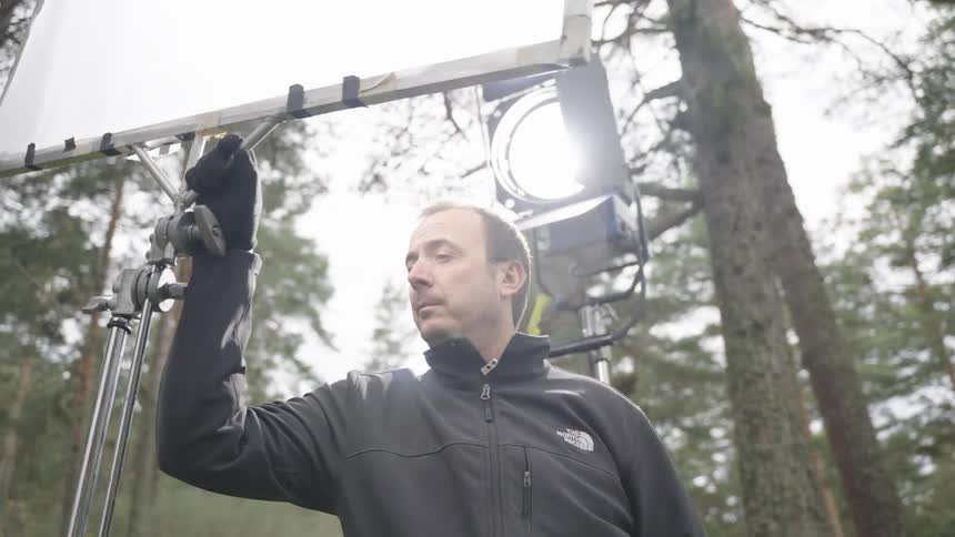A man is operating lighting on the film shoot