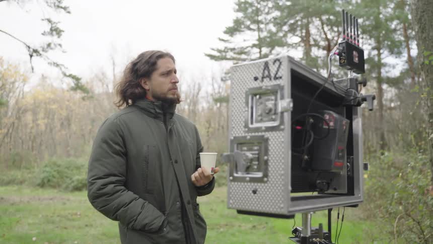 Man watching a filming on a recording screen on a site with other people participating in the middle of the forest